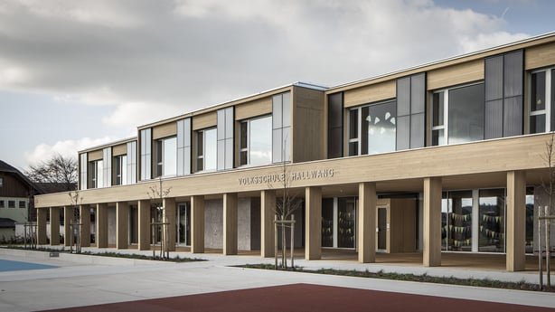 Außenansicht der Volksschule Hallwang. Das moderne, vollsolar beheizte Schulgebäude hat eine in die Fassade integrierte Solaranlage und einen großzügigen Vorplatz.