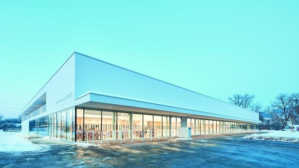 Außenansicht des Sportzentrums Nord im Winter. Das moderne, weiße Plus-Energie-Gebäude mit großer Glasfassade wird mit Abwärme der nahen Kunsteisbahn beheizt.