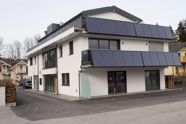Außenansicht des solar beheizten Büro- und Wohnhauses in Grödig. Das moderne, weiße Gebäude verfügt über eine große, in die Fassade integrierte Solaranlage.