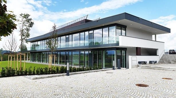 Außenansicht des modernen Kulturzentrums Hallwang. Das Plusenergie-Gebäude verfügt über eine große Glasfassade und eine Photovoltaik-Anlage auf dem Dach.